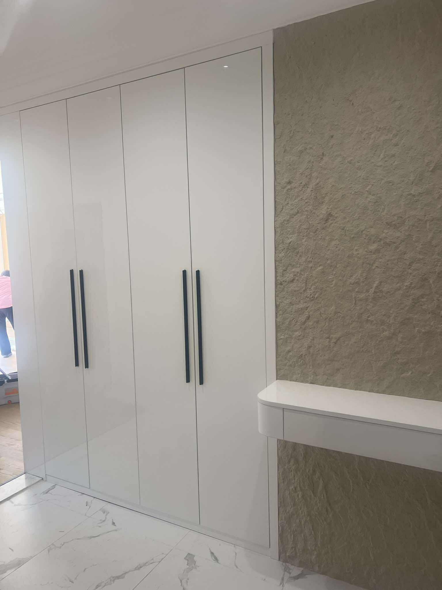 White gloss wardrobe beside textured stone wall