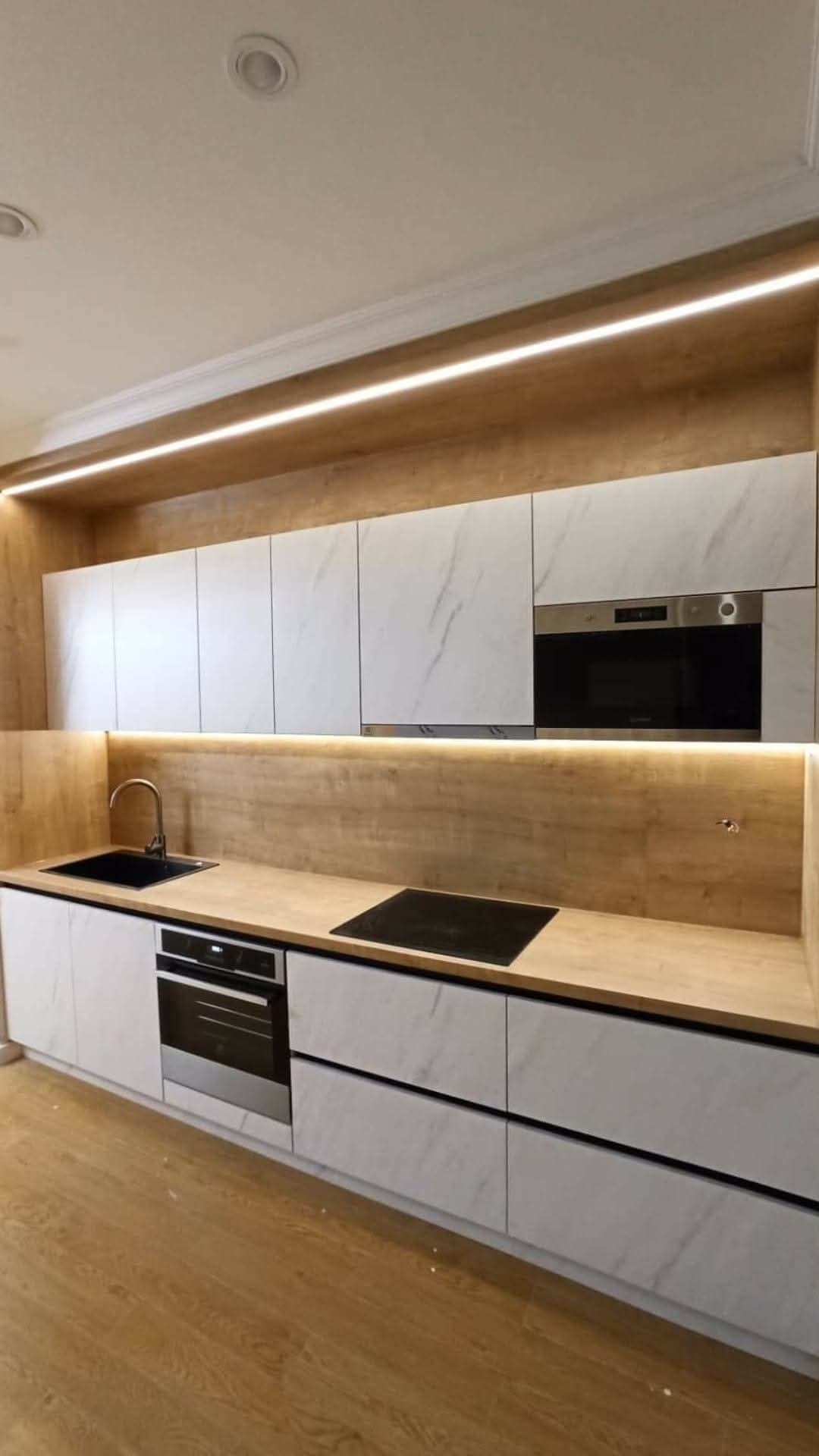 White kitchen with wood backsplash and linear LED lighting